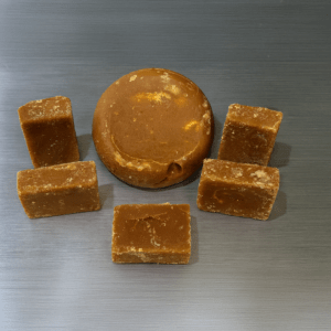 Tariango panela product surrounded by brown sugar cubes, vibrant bird decor, and limes, set against a sugarcane field backdrop, highlighting its natural origins.