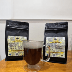 Brewed coffee in a clear glass cup, placed in front of two bags of Tarrazu Food single-origin coffee, highlighting the product for coffee enthusiasts.