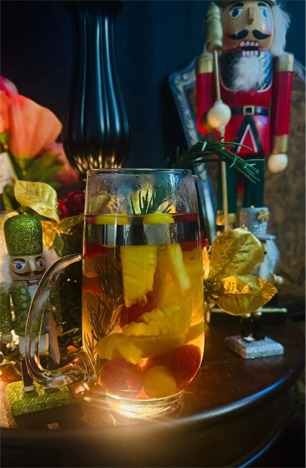 A glass of fruit-infused drink sits on a table, surrounded by festive decorations, including a nutcracker and colorful foliage.